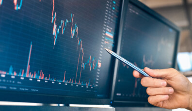 Man trader sitting at desk at office in front of monitors with stocks data pointing at screen with pen analyzing and interpreting candle chart cryptocurrency exchange close-up